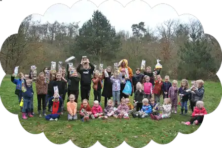 Groepsfoto van de kinderen bij het paaseieren zoeken, met hun gevonden zakjes paaseieren omhoog.